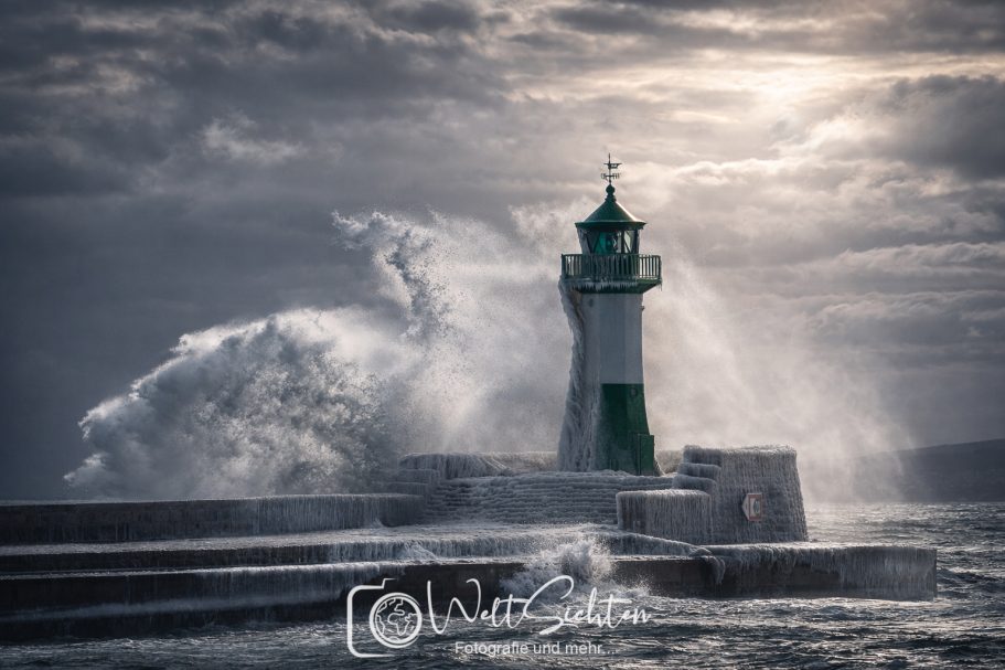 Leuchtturm Sassnitz im Wintersturm auf Rügen Leuchtturm an einer Küste mit hohen Wellen und dramatischem Himmel.