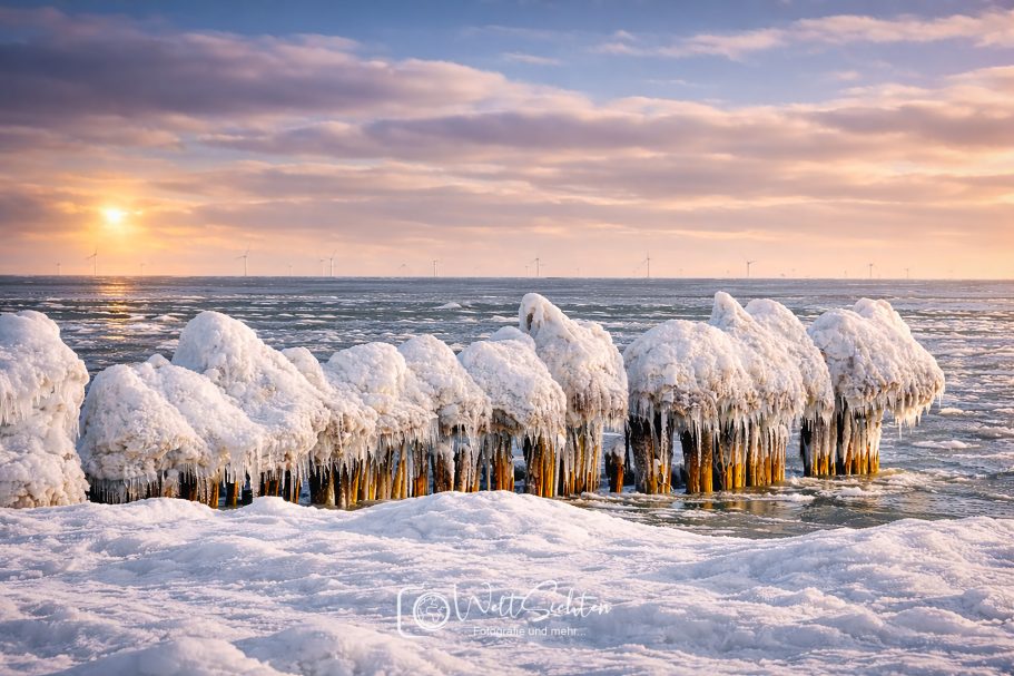 Eiszauber an der Ostseeküste auf Rügen Eingefrorene Wellenbrecher im Schnee, mit Sonnenuntergang am Horizont.
