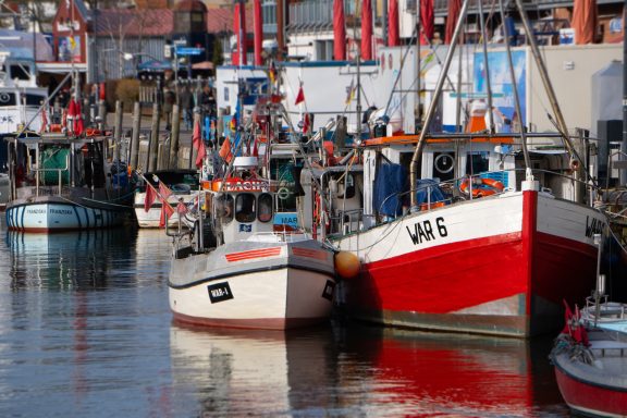Warnemünde am alten Strom Bunte Boote in einem Hafen mit Waren und Blick auf die Uferanlagen.